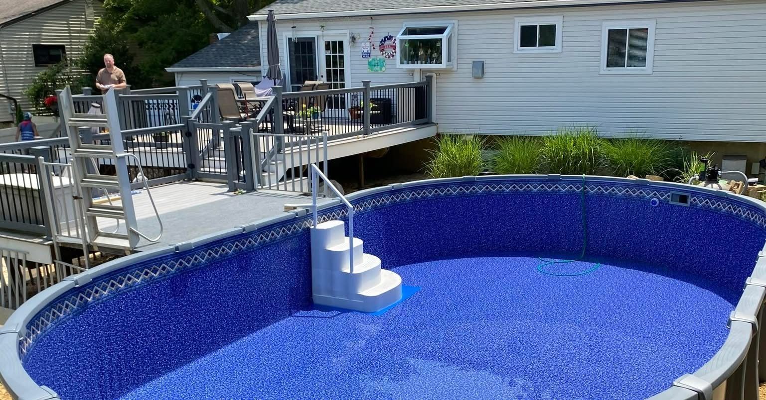 A large swimming pool is sitting on top of a wooden deck next to a house.