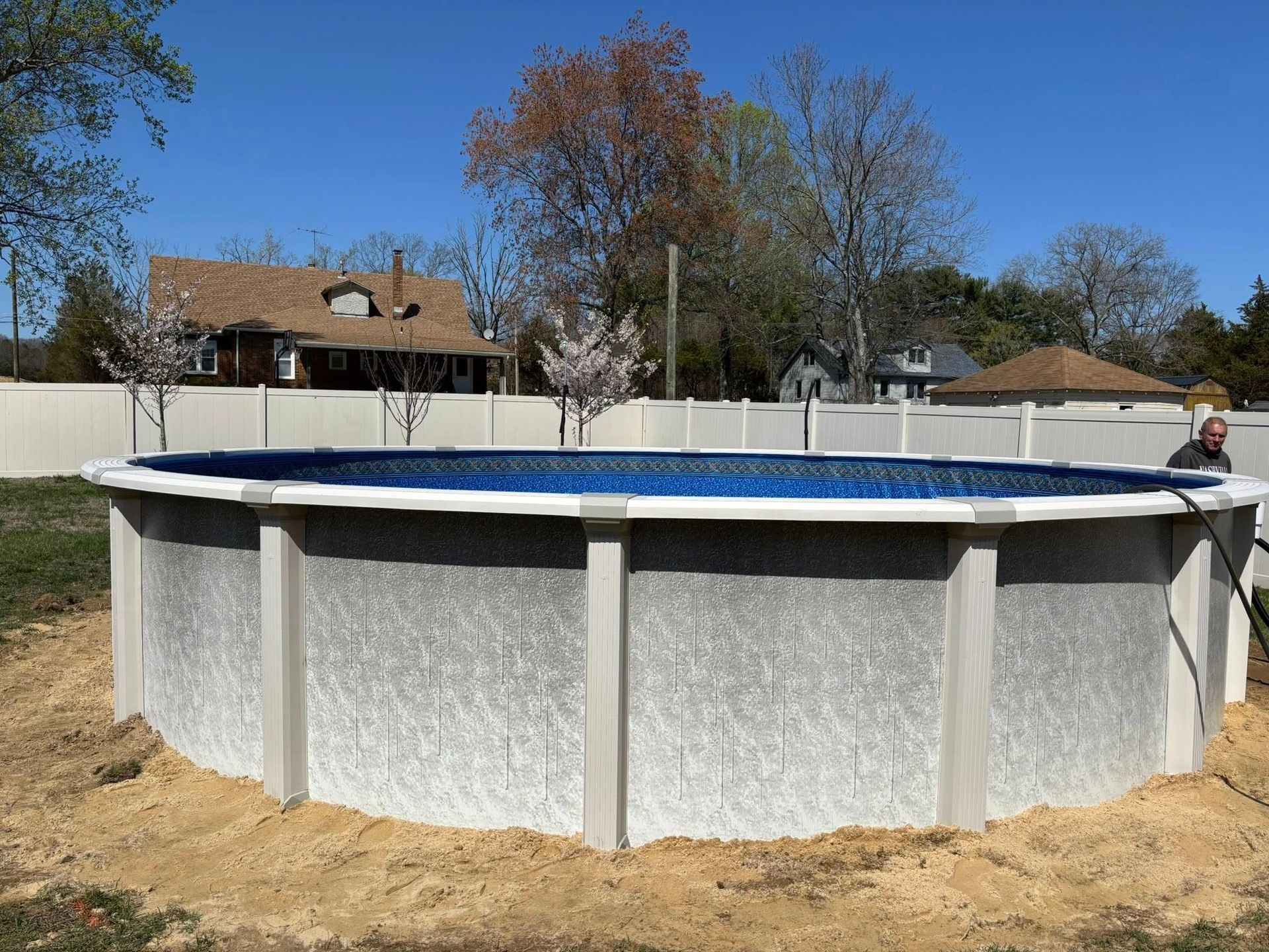 A man is standing next to a large swimming pool in a backyard.