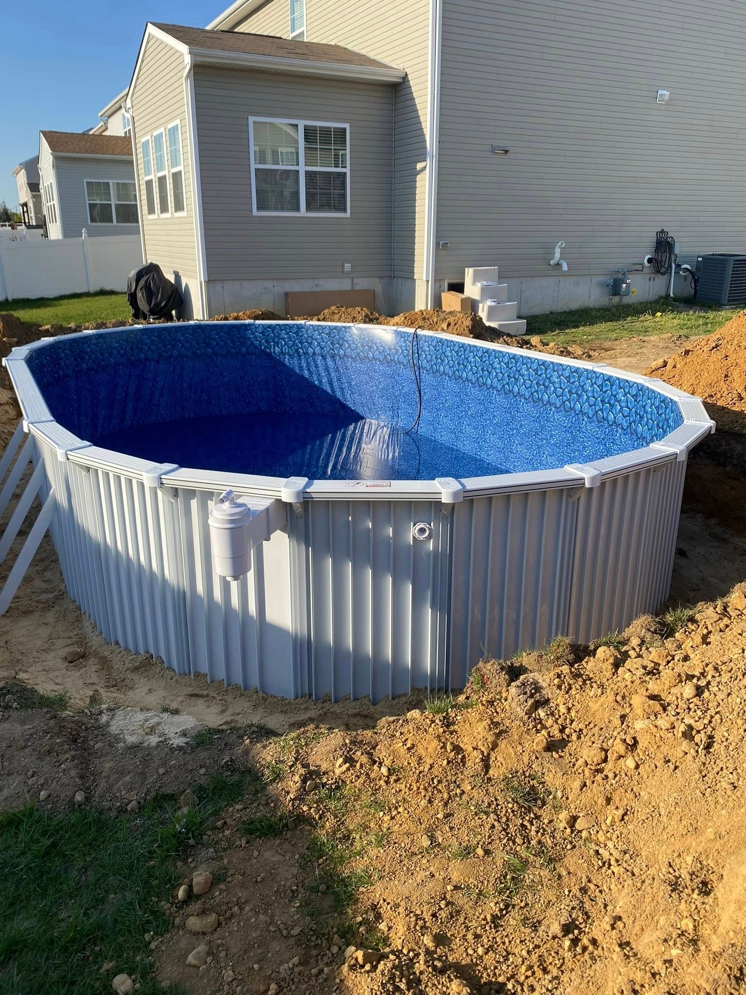 An oval swimming pool is being built in the backyard of a house.