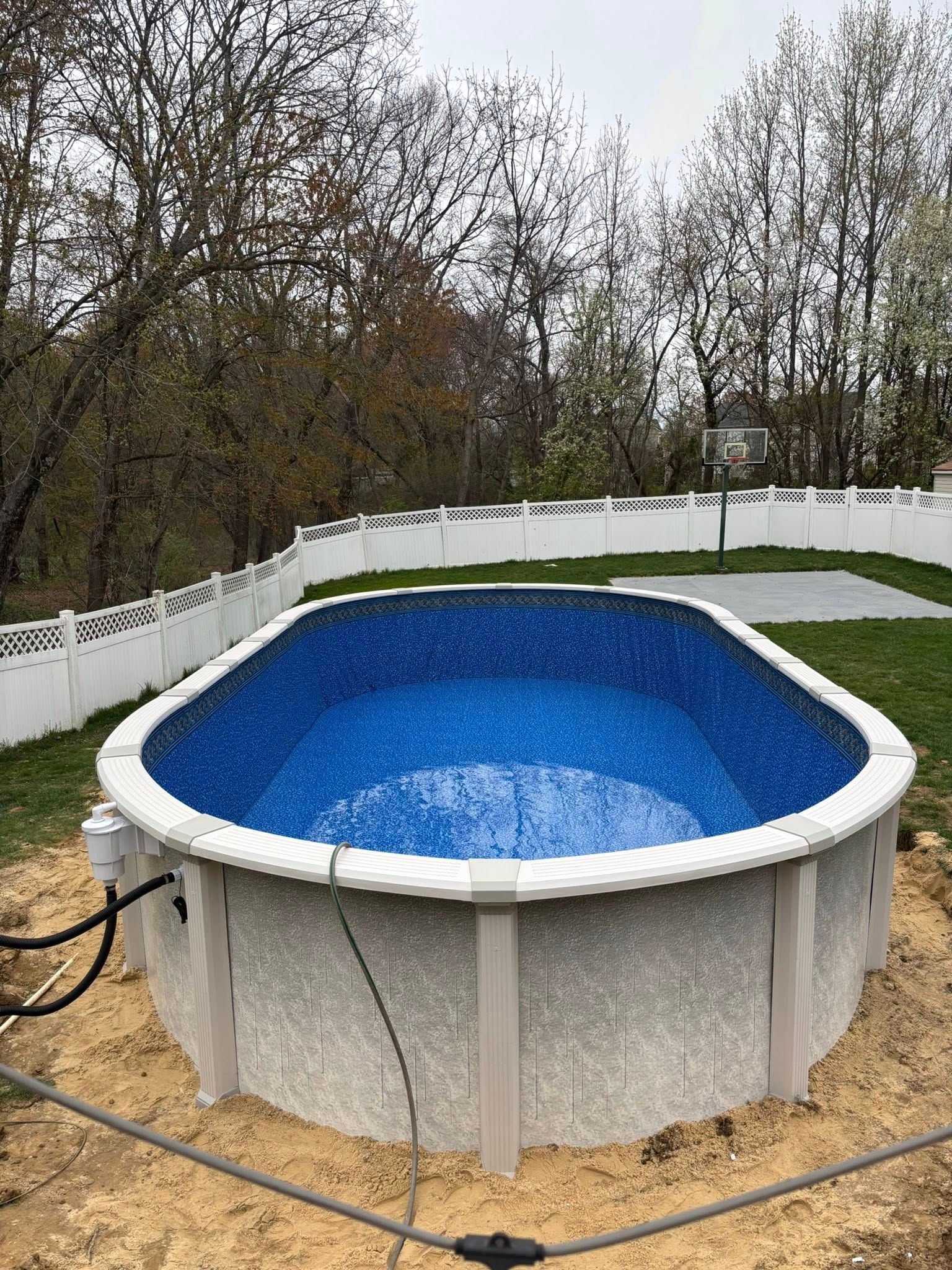 A swimming pool is sitting in the middle of a backyard next to a white fence.