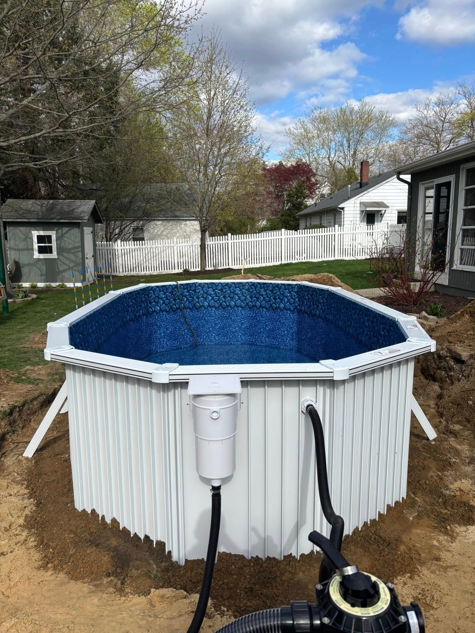 A white pool is sitting in the dirt next to a house.
