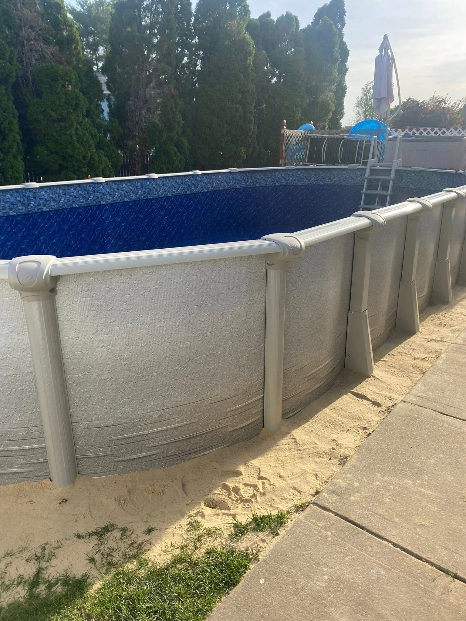 A large swimming pool is sitting on top of a concrete patio next to a sidewalk.