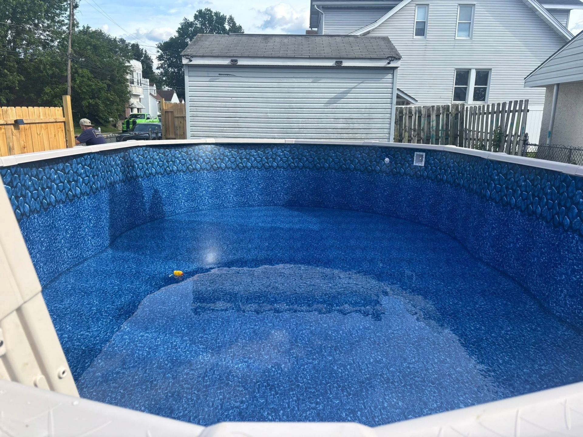 A large blue swimming pool is sitting in front of a house.