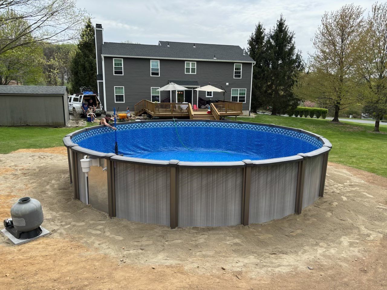 A large swimming pool is sitting in the dirt in front of a house.