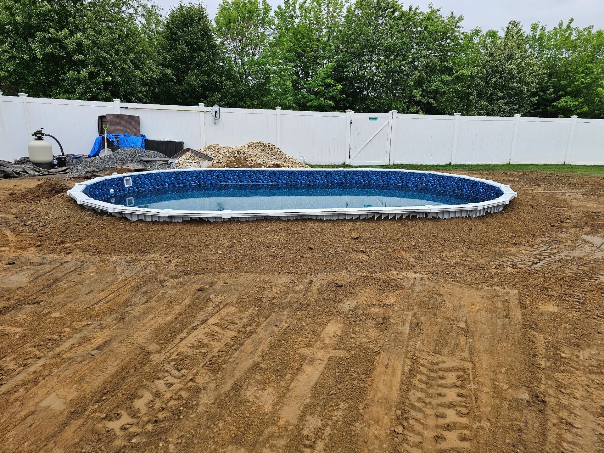 An oval swimming pool is being built in a dirt yard.