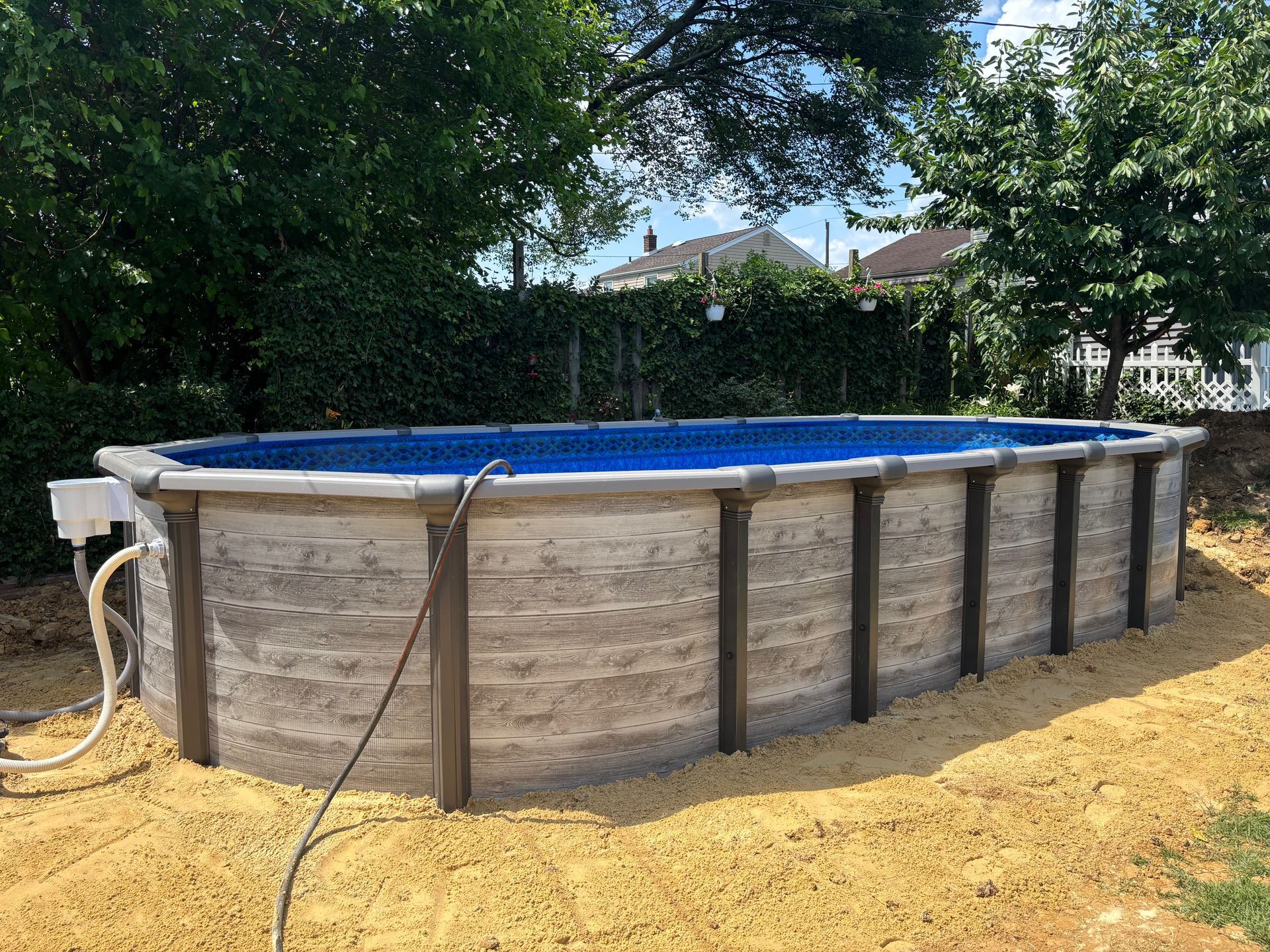A large swimming pool is sitting in the dirt in a backyard.