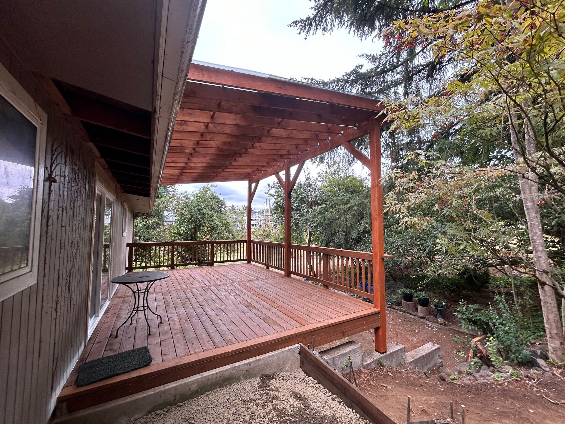 A pergola with chairs and a table in a backyard.