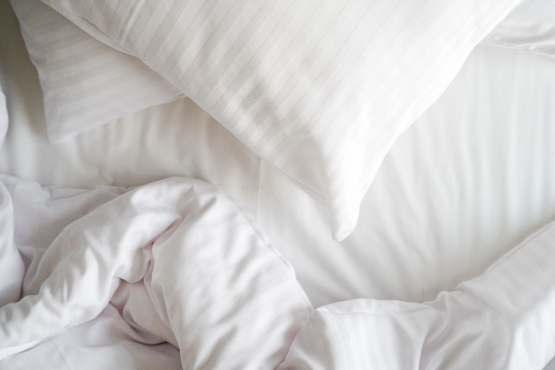 Letto bianco con lenzuola stropicciate e due cuscini.