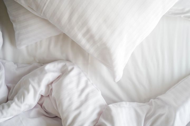 Letto bianco con lenzuola stropicciate e due cuscini.