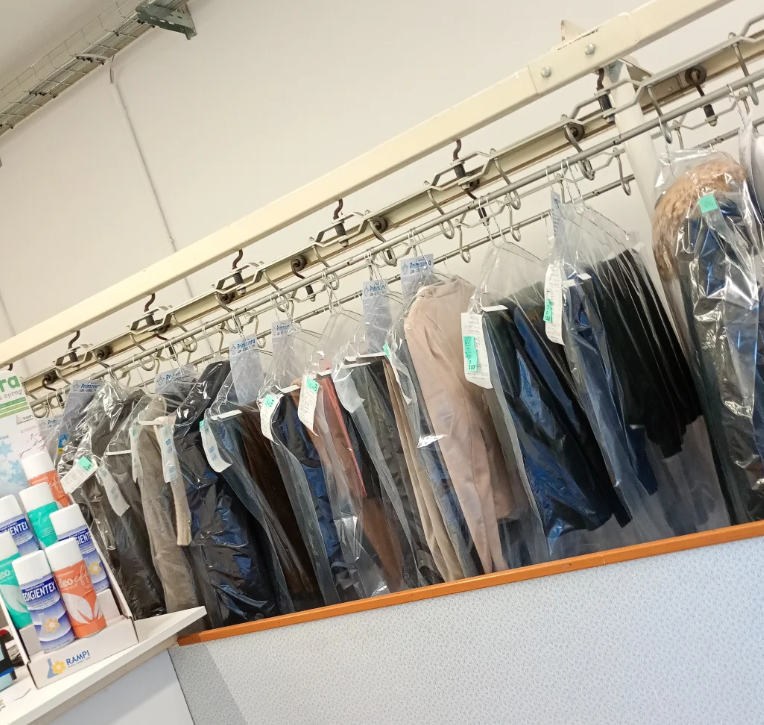 Vestiti appesi in sacchetti protettivi in ​​una lavanderia a secco, probabilmente dopo la pulizia, con i prodotti in primo piano.