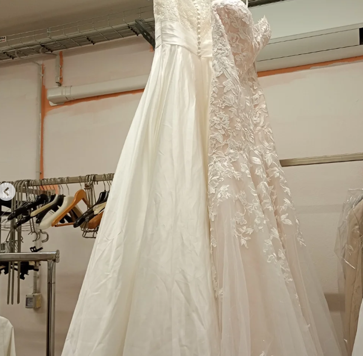 Due abiti da sposa bianchi appesi su un attaccapanni. Uno ha dettagli in pizzo.