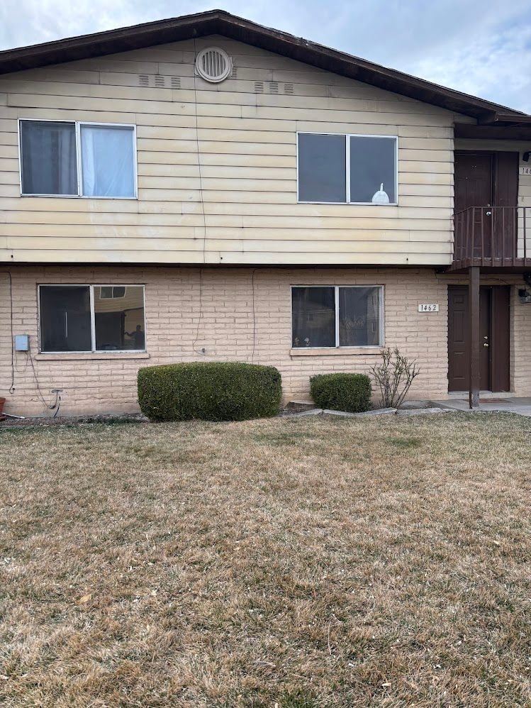 Two-story apartment building with tan siding over brick, brown door, and dry lawn in front.
