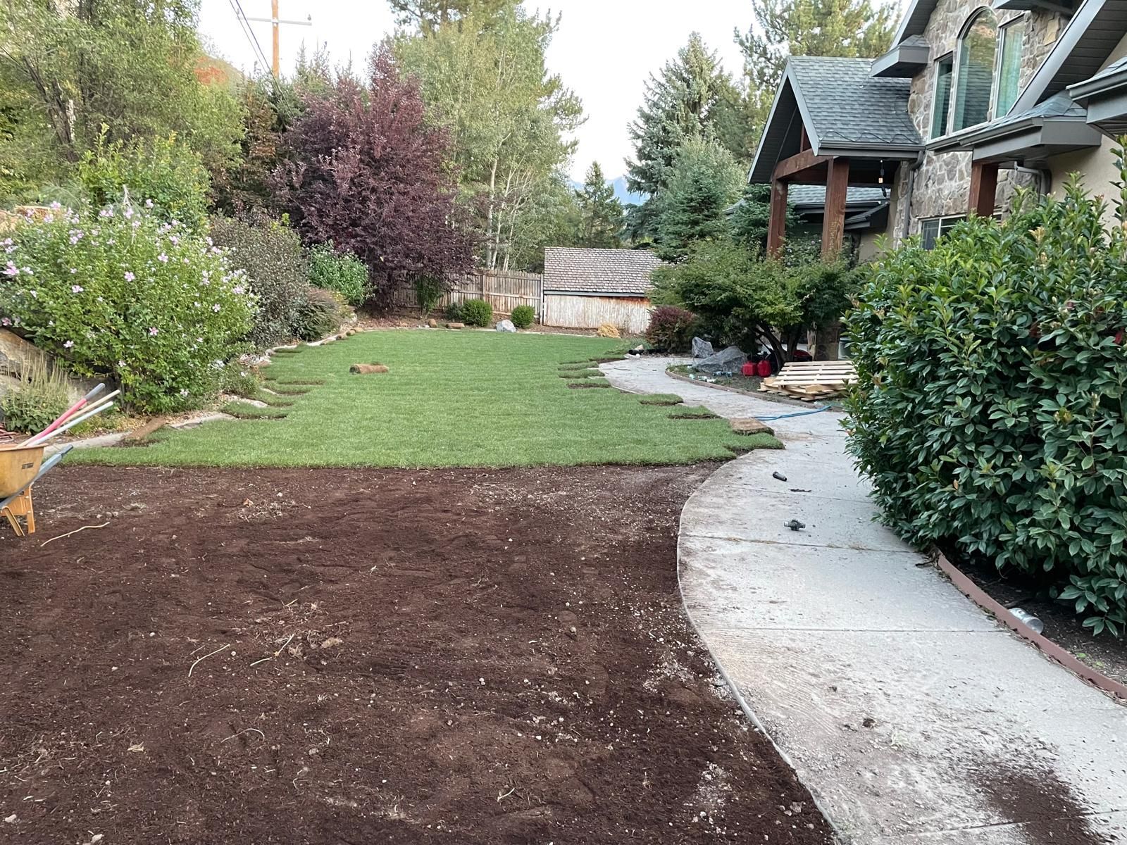 A person is spreading mulch on a lush green lawn in front of a house.