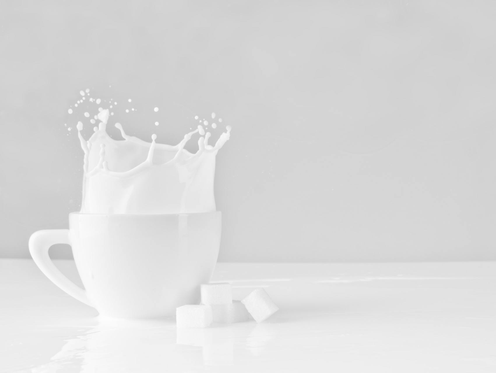 White cup with milk splashing, sugar cubes on reflective surface.
