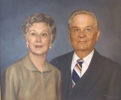 Portrait of a couple: woman in tan jacket, man in suit. They both smile at the viewer.