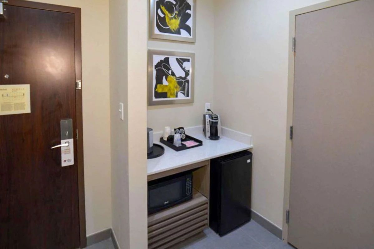 Hotel room alcove with microwave, mini-fridge, coffee station, art, and a door.