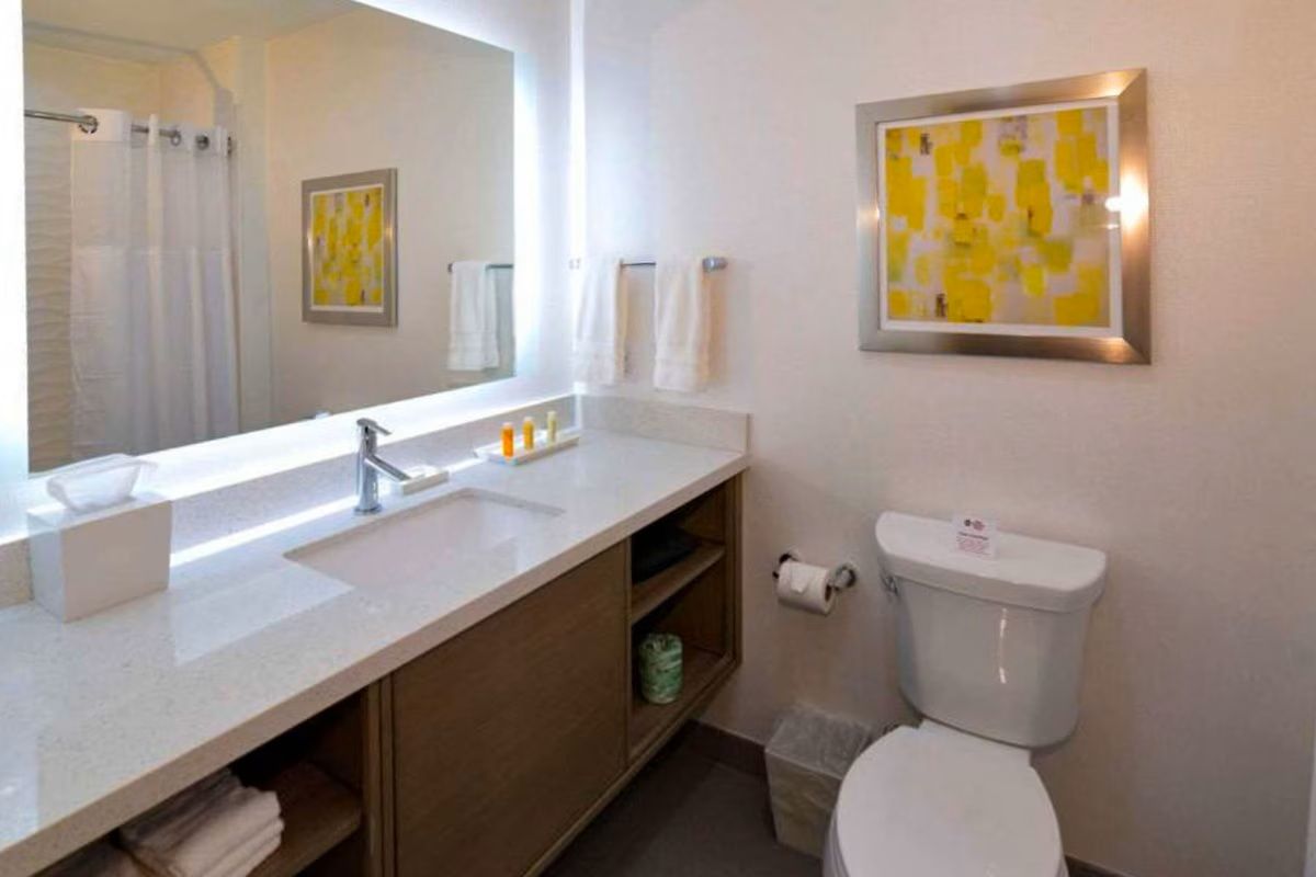 Bathroom with white sink, toilet, and artwork; tan vanity with shelving.