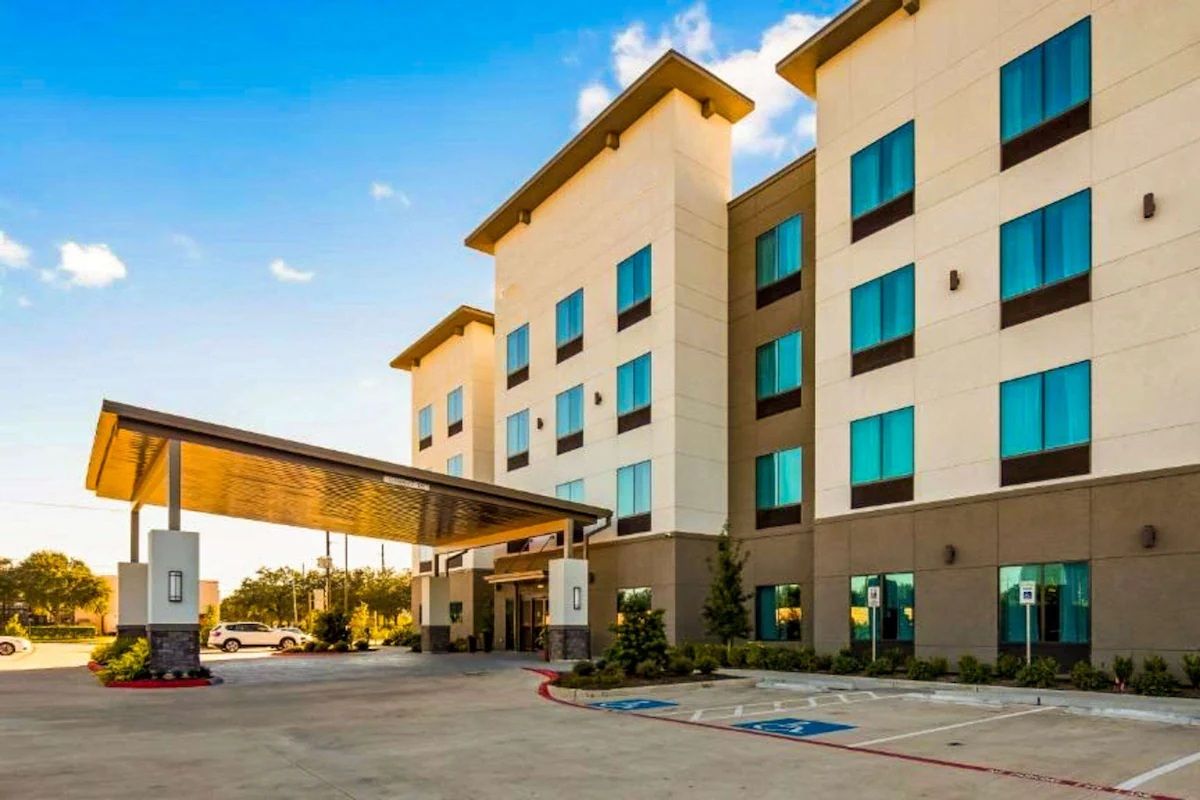 Hotel exterior with a covered entrance and blue-tinted windows against a blue sky.
