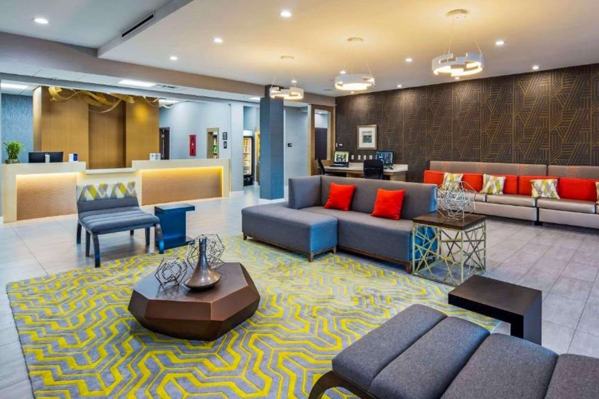 Hotel lobby with seating area and front desk. Gray, yellow, and orange accents.