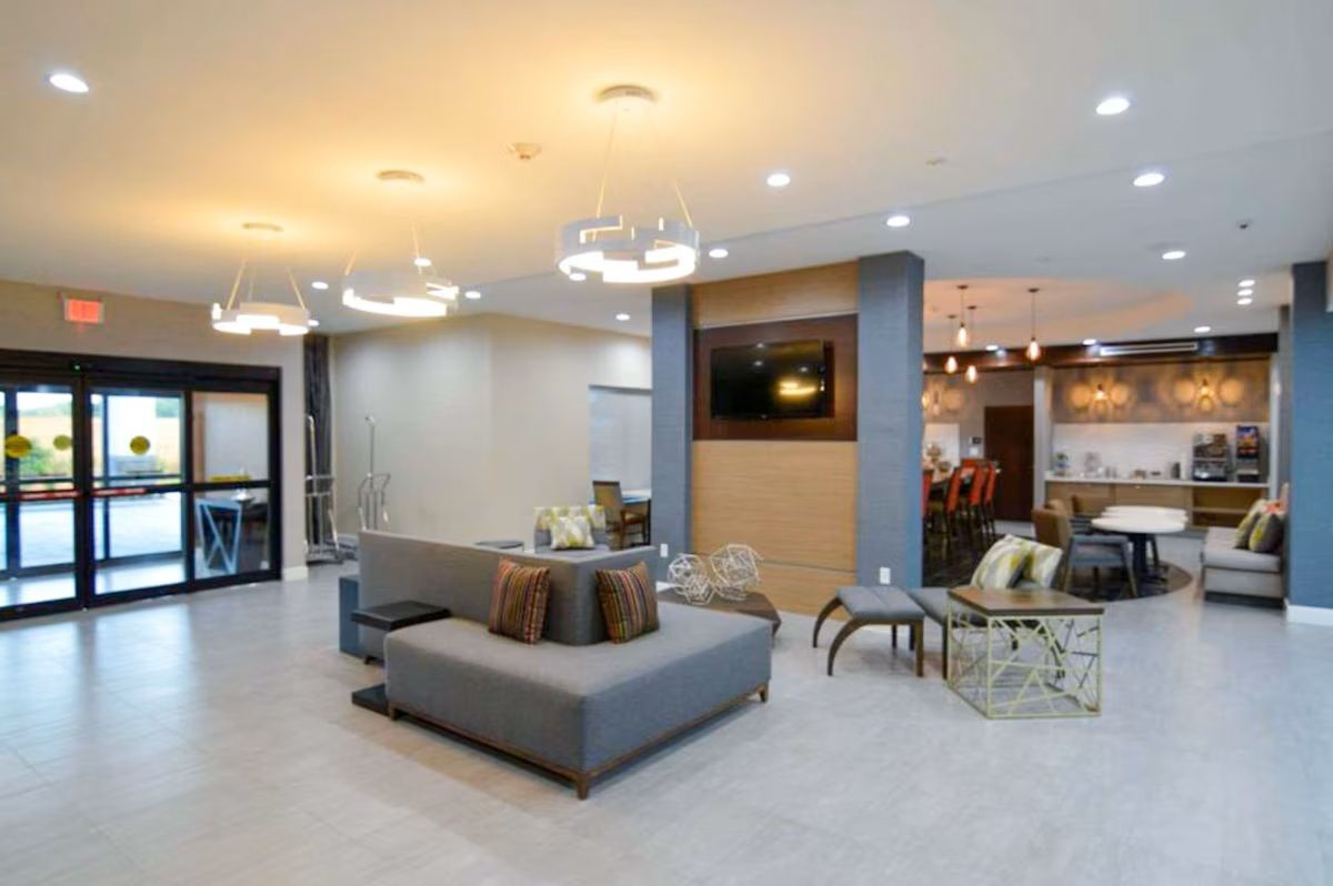 Hotel lobby with seating area, coffee station, and entrance. Gray and neutral colors.