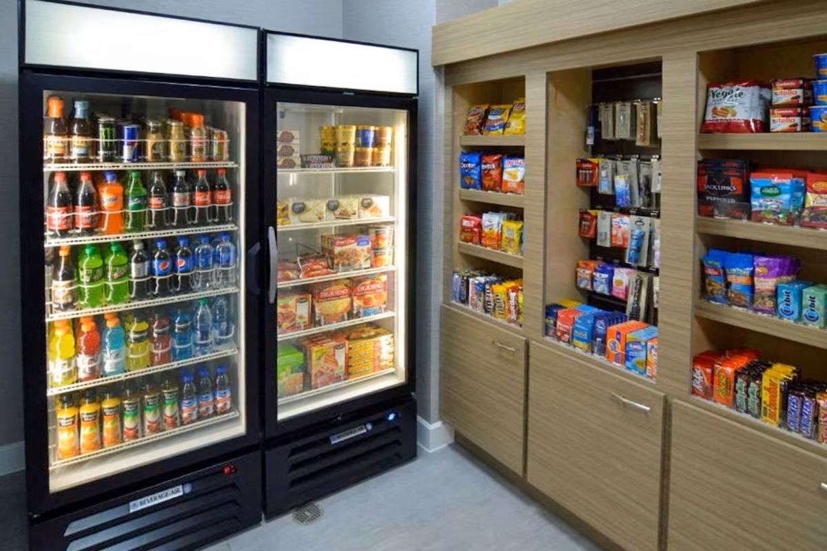 Refrigerated beverage and snack display with shelf storage in a brightly lit room.
