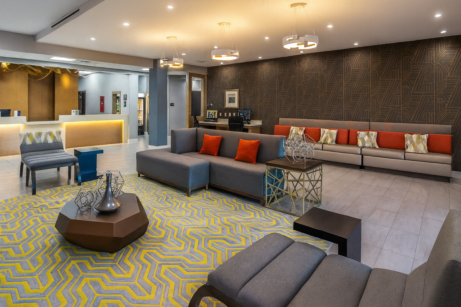Hotel lobby with modern furniture, gray and orange accents, yellow patterned rug, and reception desk.