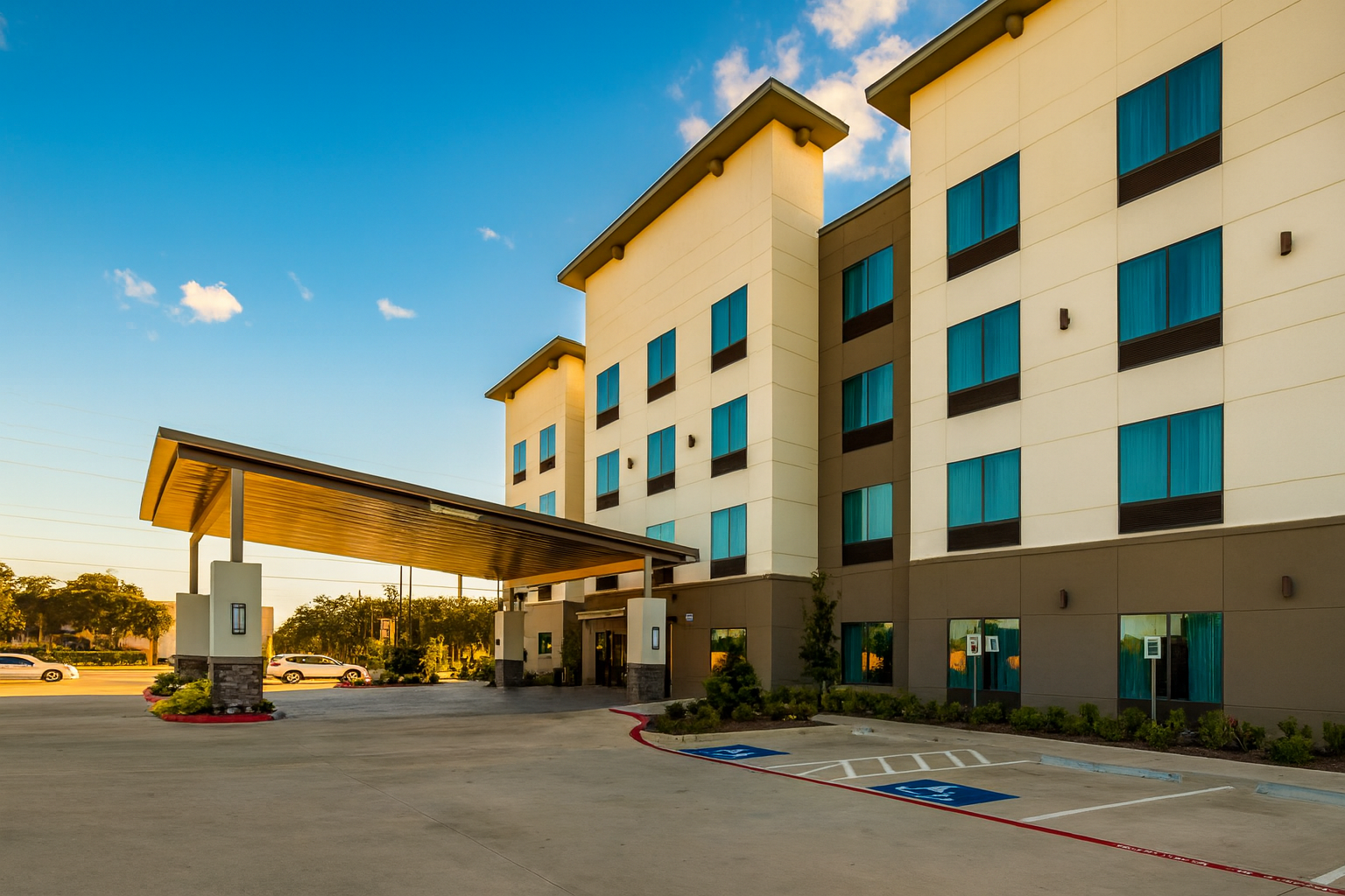 Modern hotel exterior with a covered entrance, blue-tinted windows, and accessible parking.
