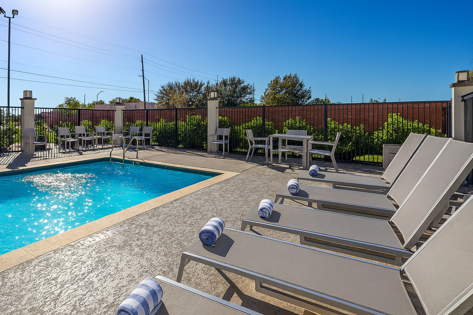 Pool with lounge chairs and tables on a sunny day.
