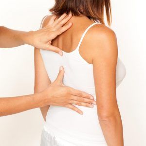 A woman in a white tank top is getting a massage from a man.