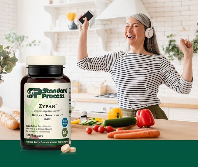 A woman is standing in a kitchen with vegetables and a bottle of zypan.