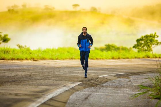 A man in a blue jacket is running down a road.