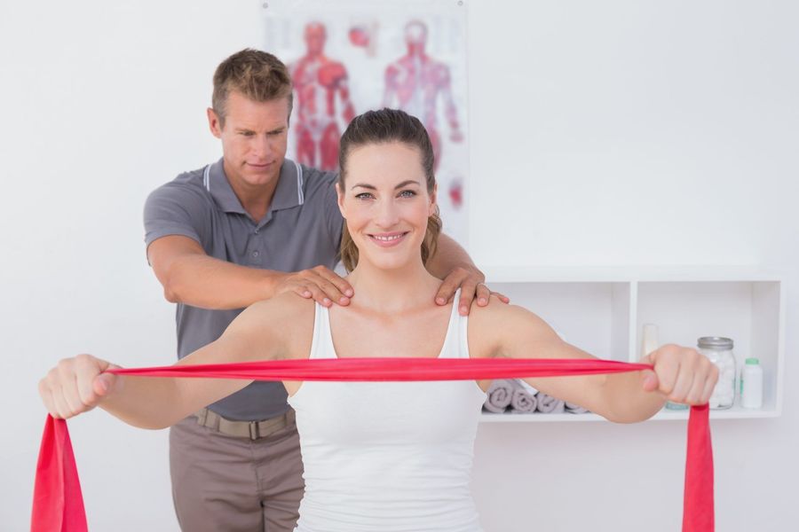 A man is helping a woman stretch her arms with a red resistance band.