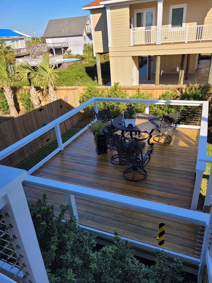 Wooden deck with black patio furniture, cable railings, and a two-story beige house.