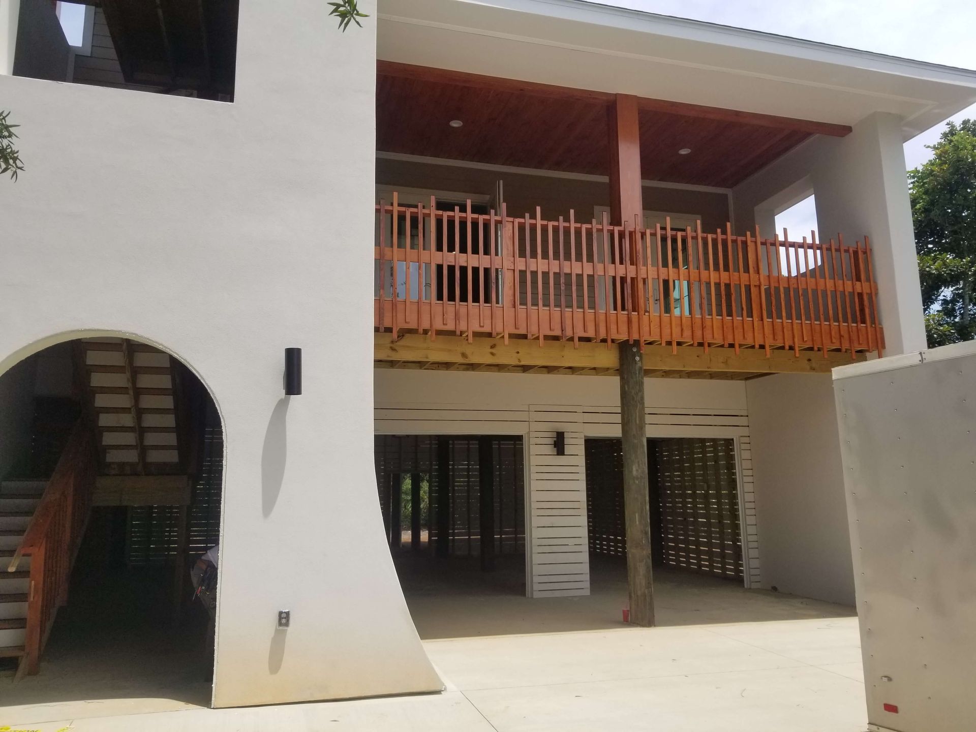 Two-story white building with a wooden balcony and stairs. Open space beneath the balcony.