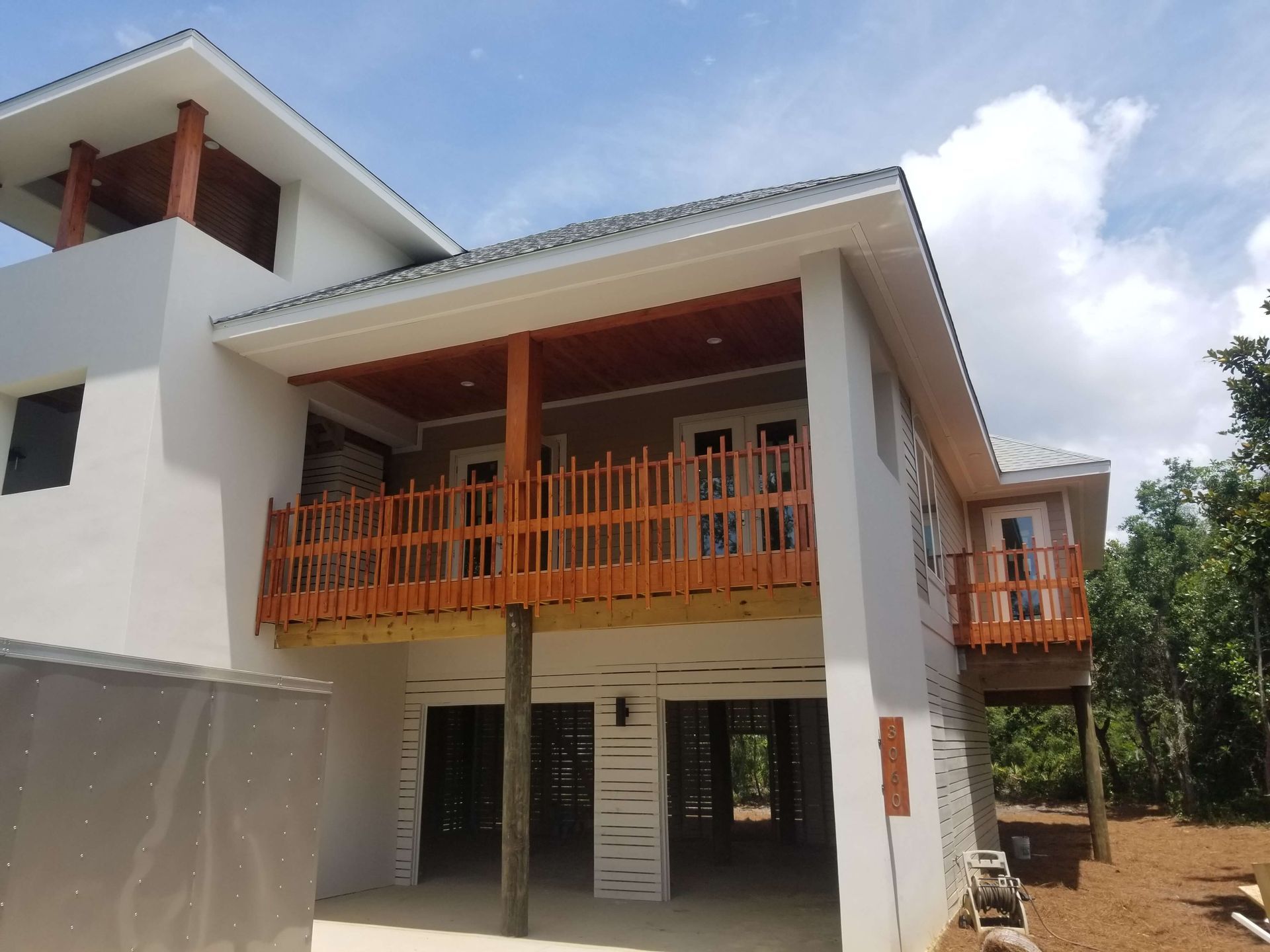 Two-story house with brown wooden accents, balcony, and partially open ground level.