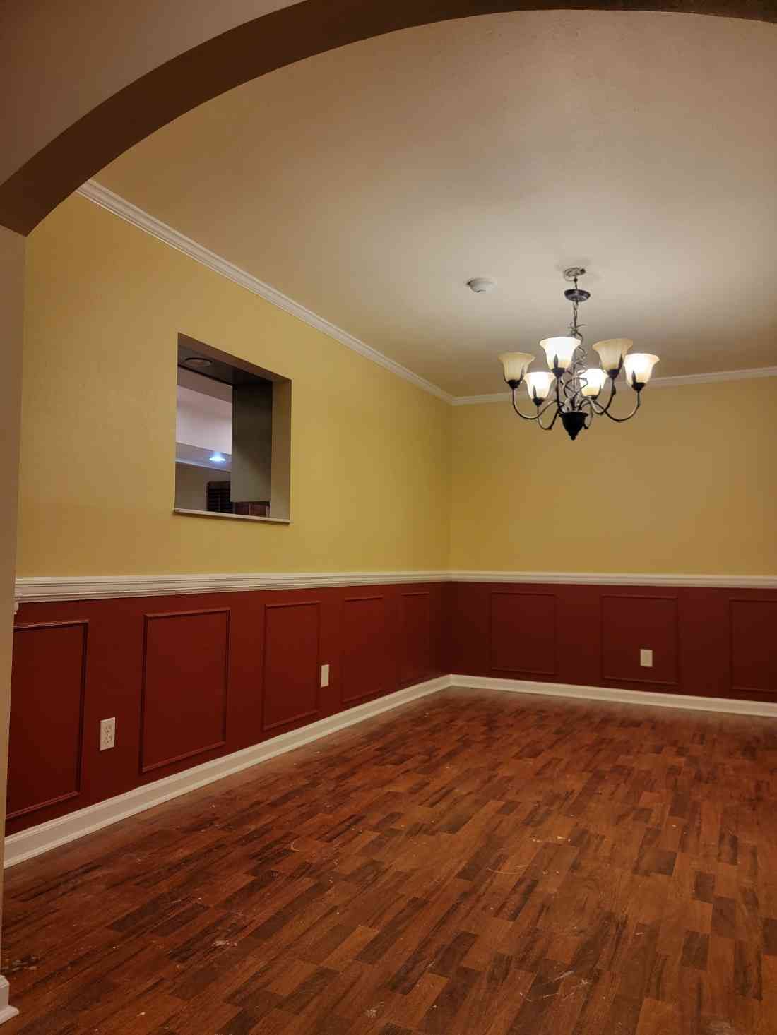 Room with dark wood floor, red paneling, yellow walls, white trim, and a chandelier.