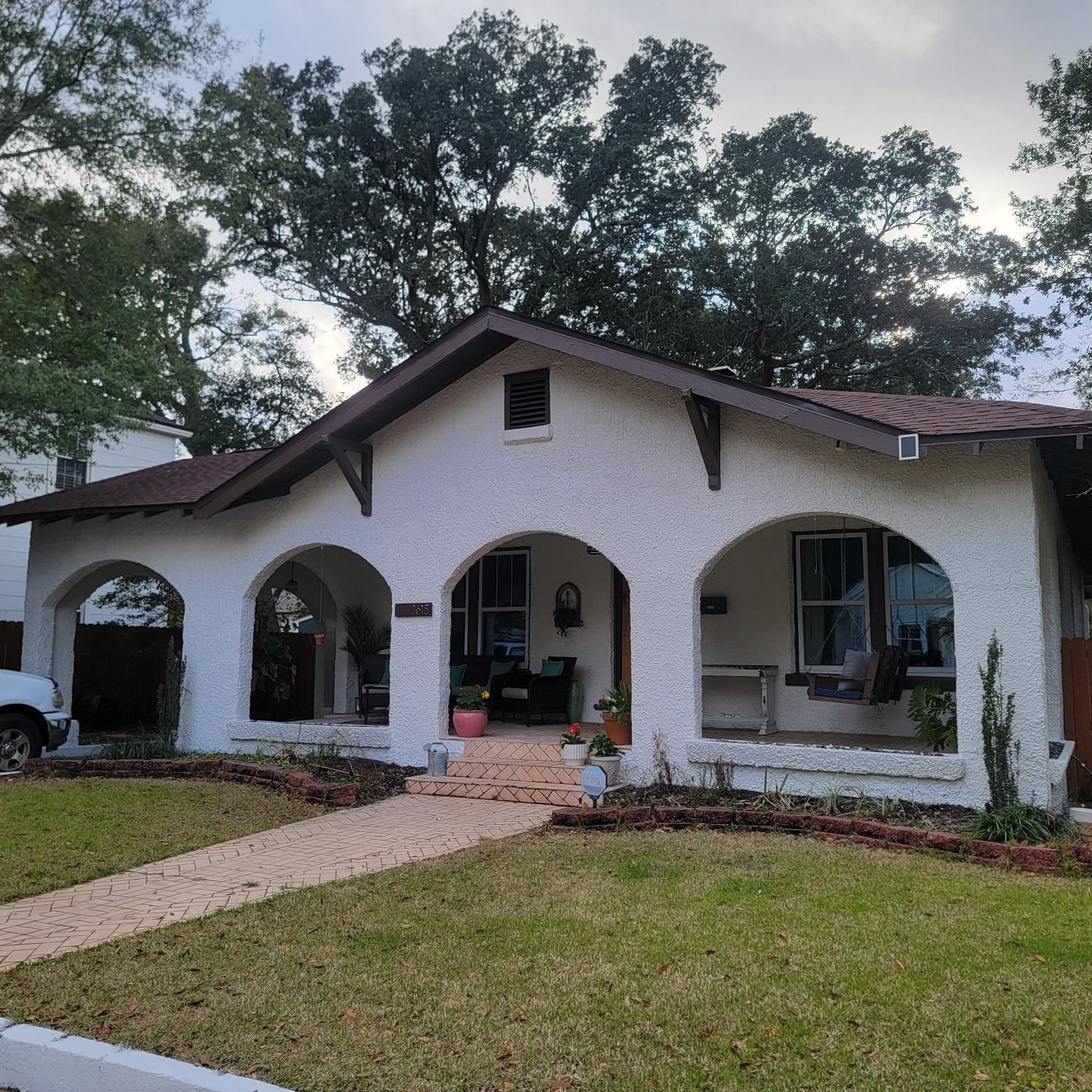 White stucco house with arched porch, brown roof, and brick walkway.