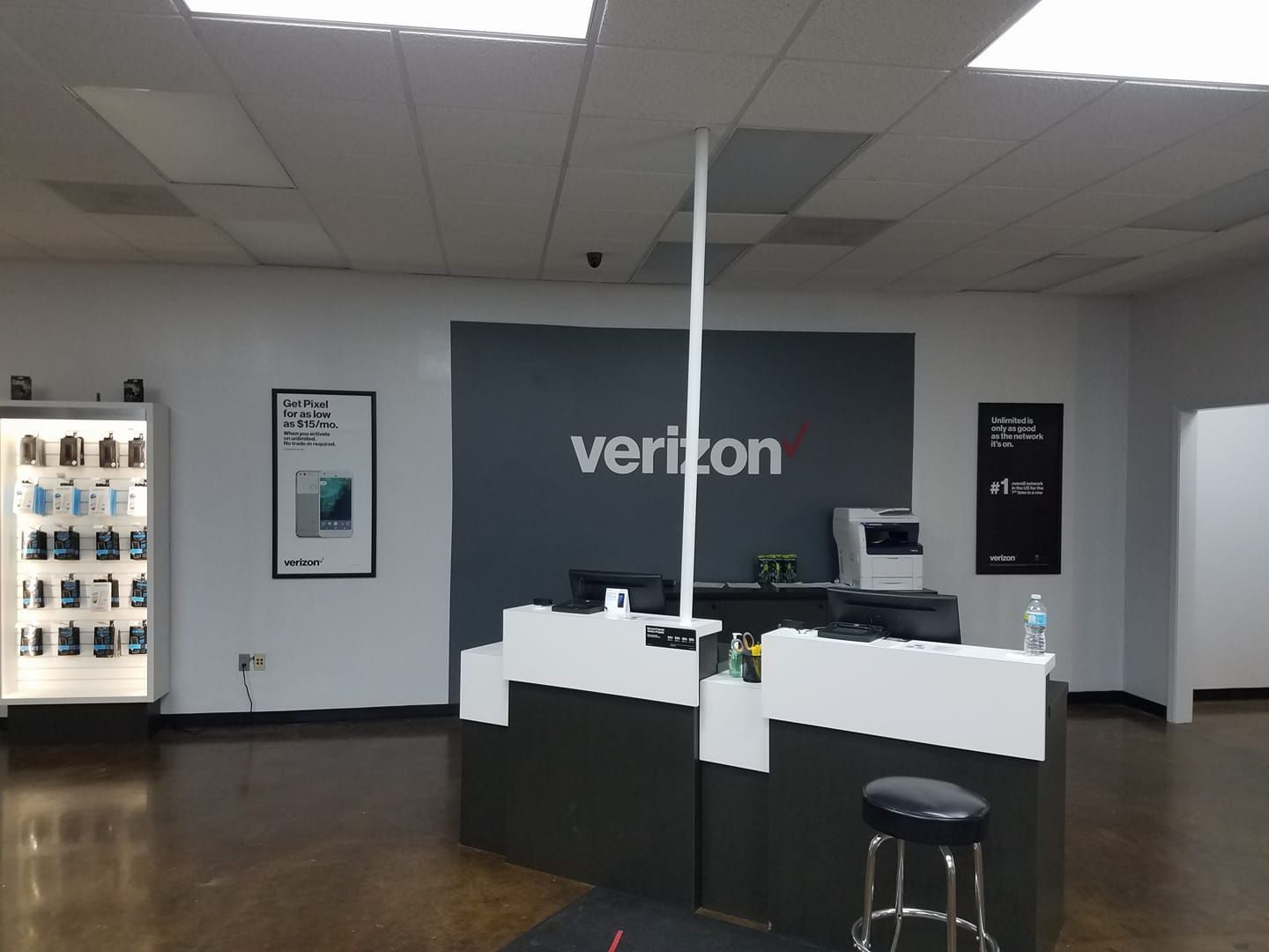 The interior of a Verizon store, featuring a service desk, a display case of accessories, and signage against a grey wall.