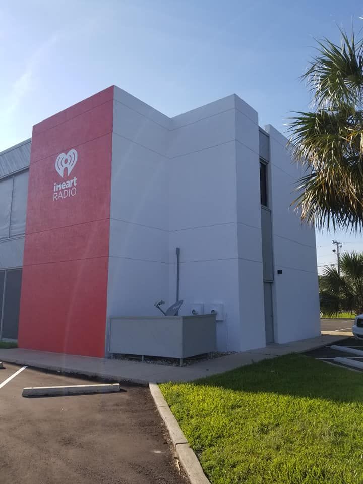 Exterior of an iHeartRadio building, red and gray with logo on side. Sunny day, palm tree in background.