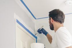 A man is kneeling down and painting a wall with a paint roller.