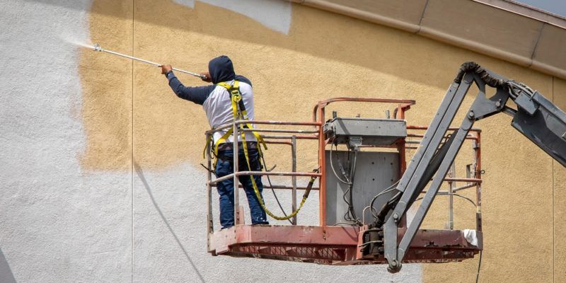 A man is kneeling down and painting a wall with a paint roller.