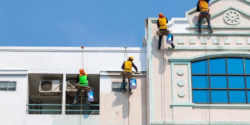 A man is kneeling down and painting a wall with a paint roller.
