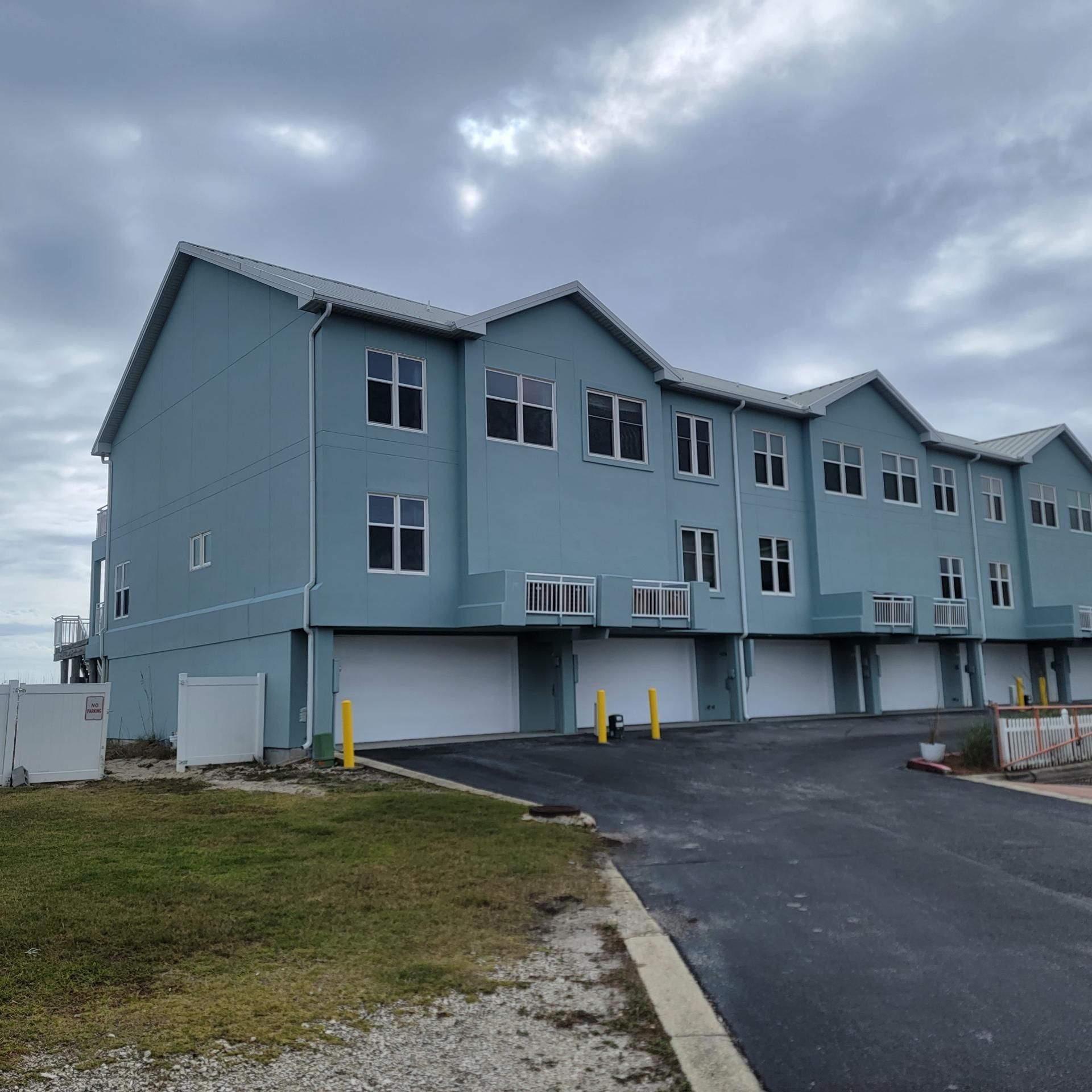 Row of blue townhouses with garages, asphalt drive, cloudy sky.