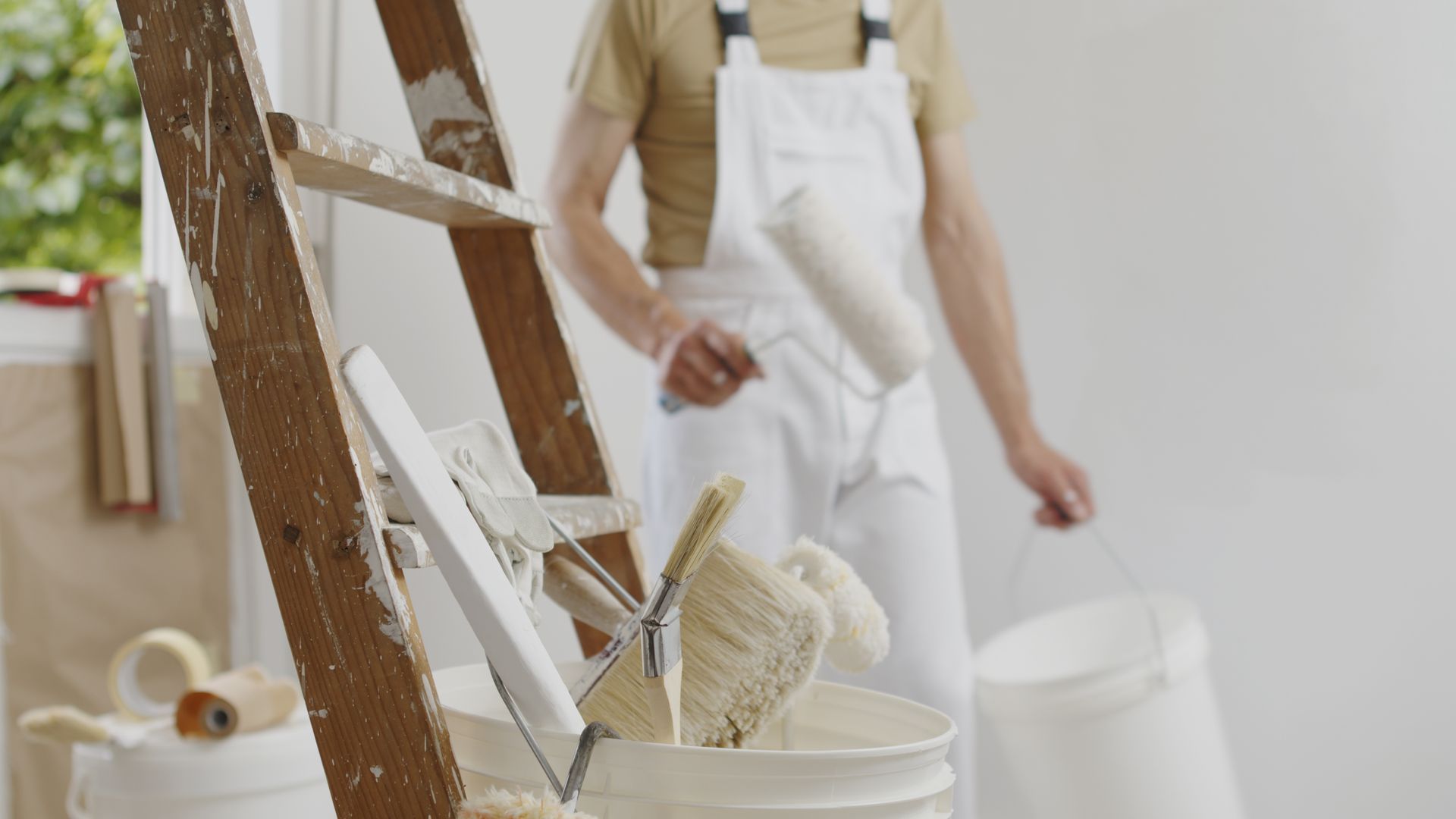 A man is kneeling down and painting a wall with a paint roller.