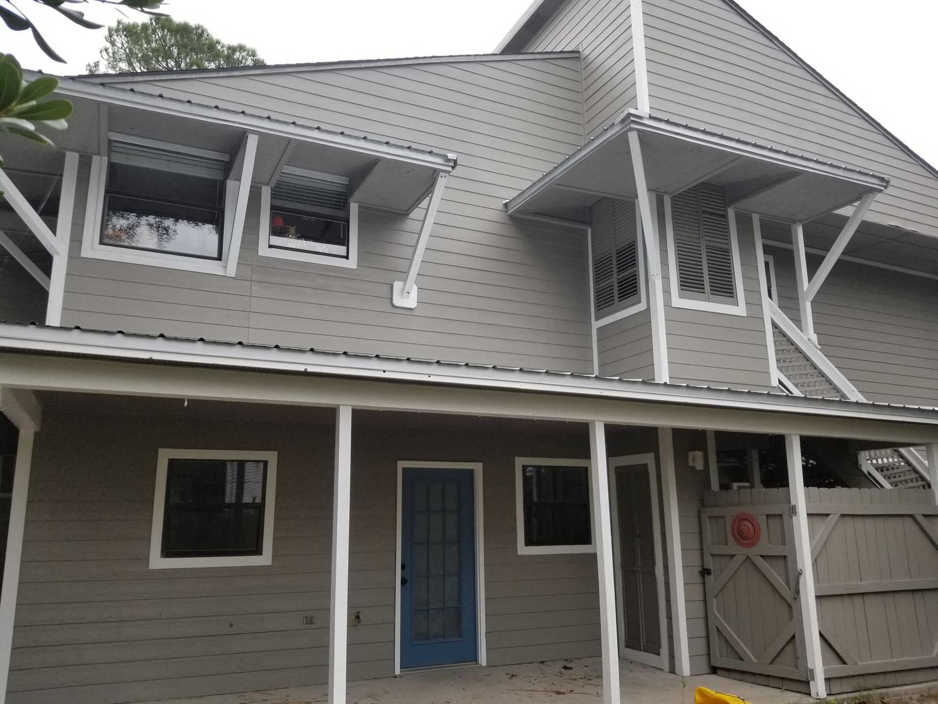 Gray house with white trim, blue door, covered porch, and windows.