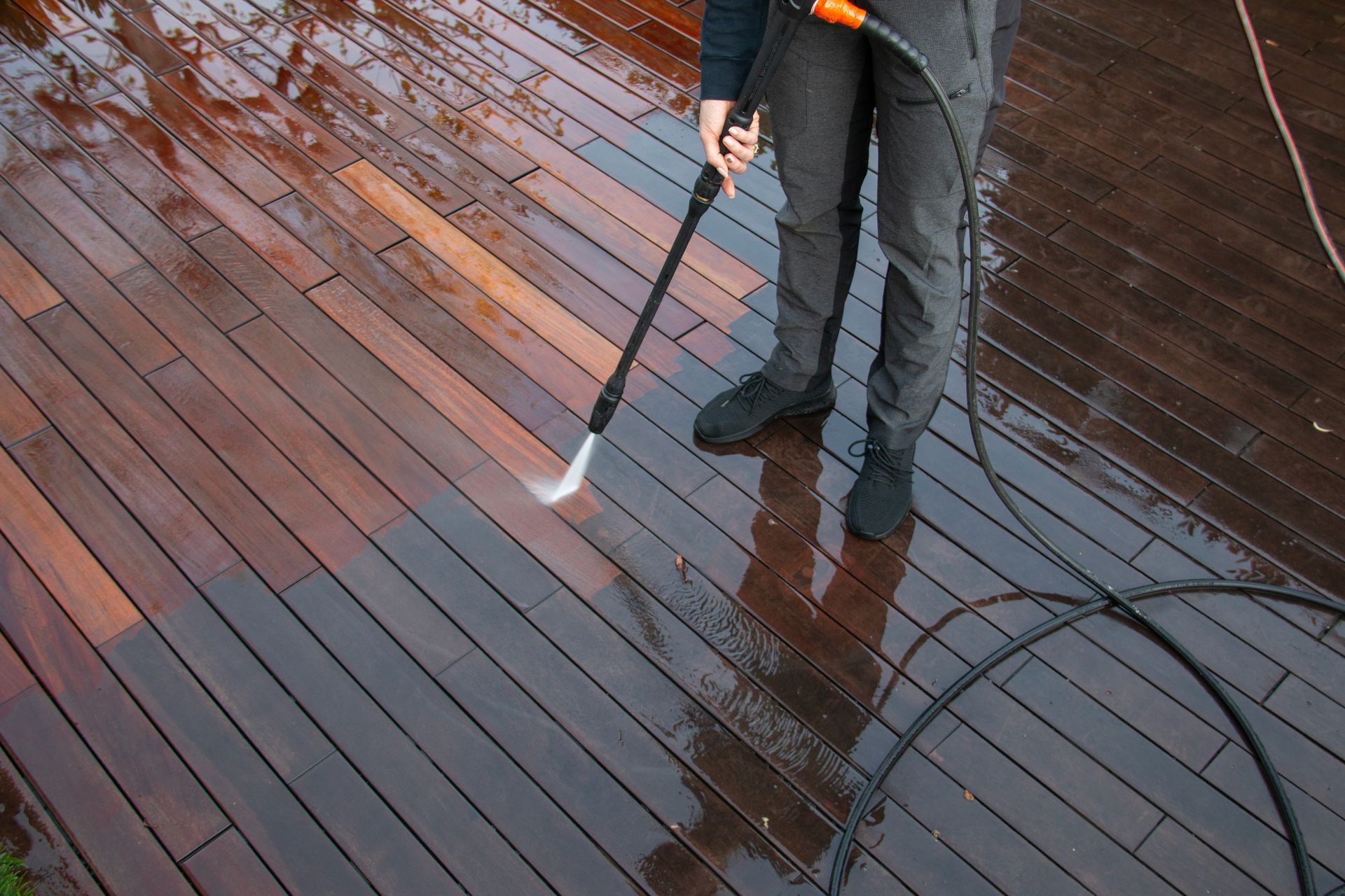 A person is using a high pressure washer to clean a wooden deck.
