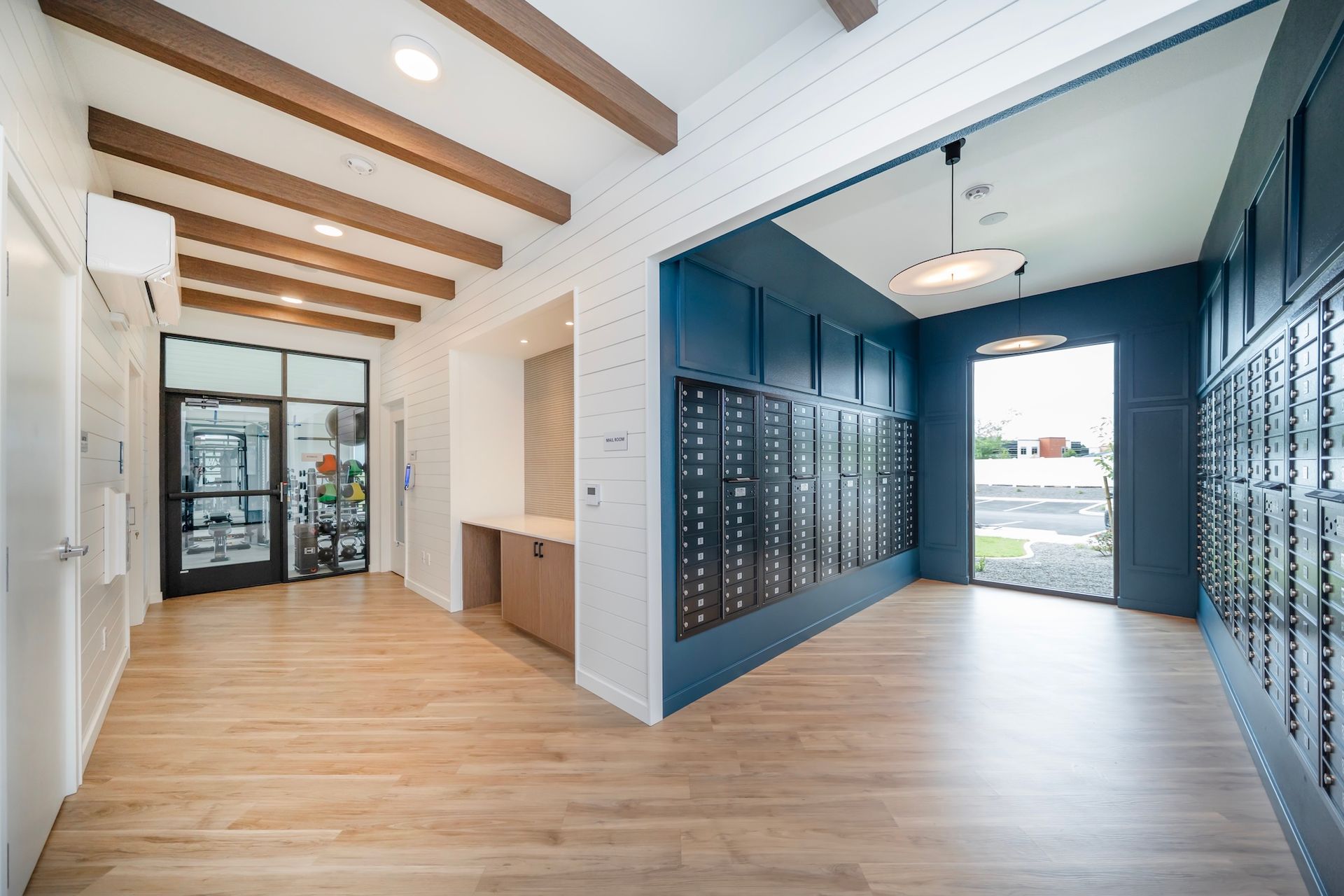 Mailbox room with blue wall and mailboxes, wooden floors and ceiling beams. Door to outside.
