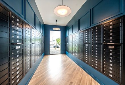 Hallway with rows of black mailboxes, teal walls, and wooden floor, leading to an open doorway.