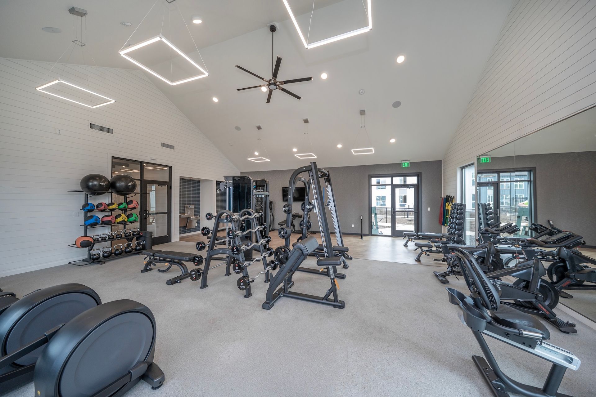 Gym with exercise equipment, including weights, machines, and cardio, in a bright space with a high ceiling.