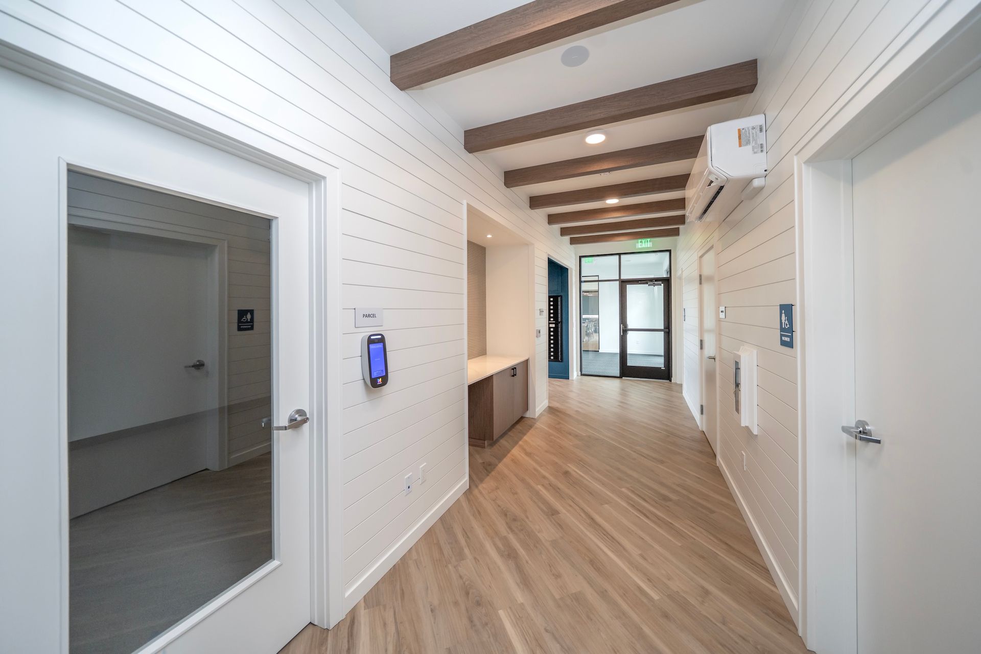 Hallway with wood-look floors and white paneled walls, leading to a glass door.